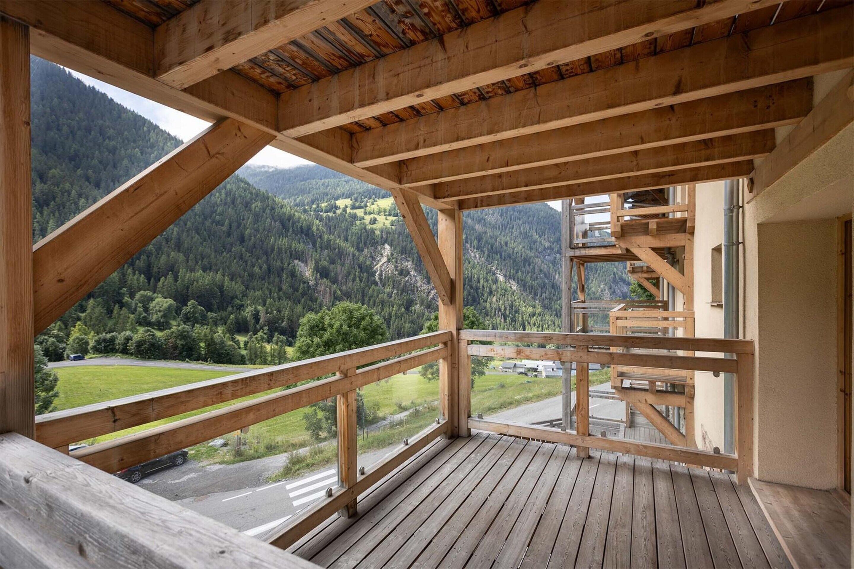 A wooden balcony with a view of a forested mountain landscape.