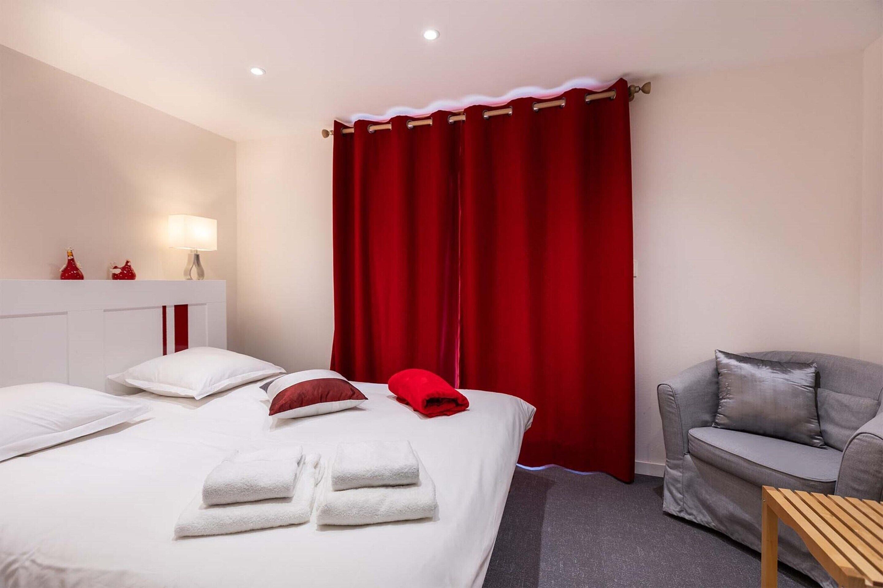 A hotel room with a bed, a sofa, a small table, and a red curtain.