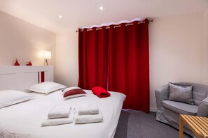 A hotel room with a bed, a sofa, a small table, and a red curtain. - Chalet in Paradiski With Spa & Stunning Views (Peisey-Nancroix)