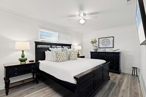 A bedroom with a bed, two nightstands, a dresser, a ceiling fan, a window with blinds, and a framed picture on the wall. - Beach House - Blueberry Beach (Panama City Beach)