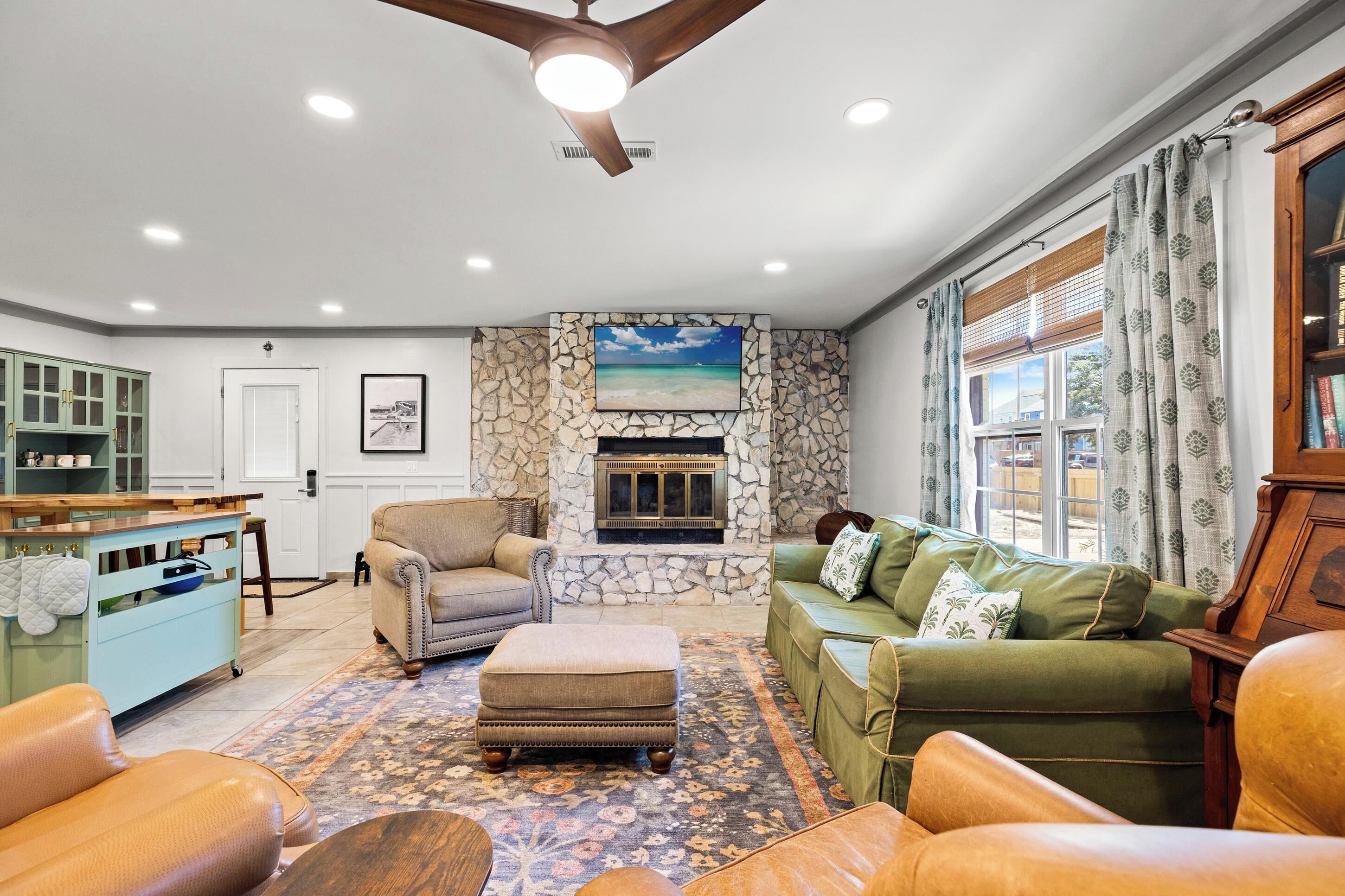 A living room with a stone fireplace, a ceiling fan, and a view of the outdoors through a window.