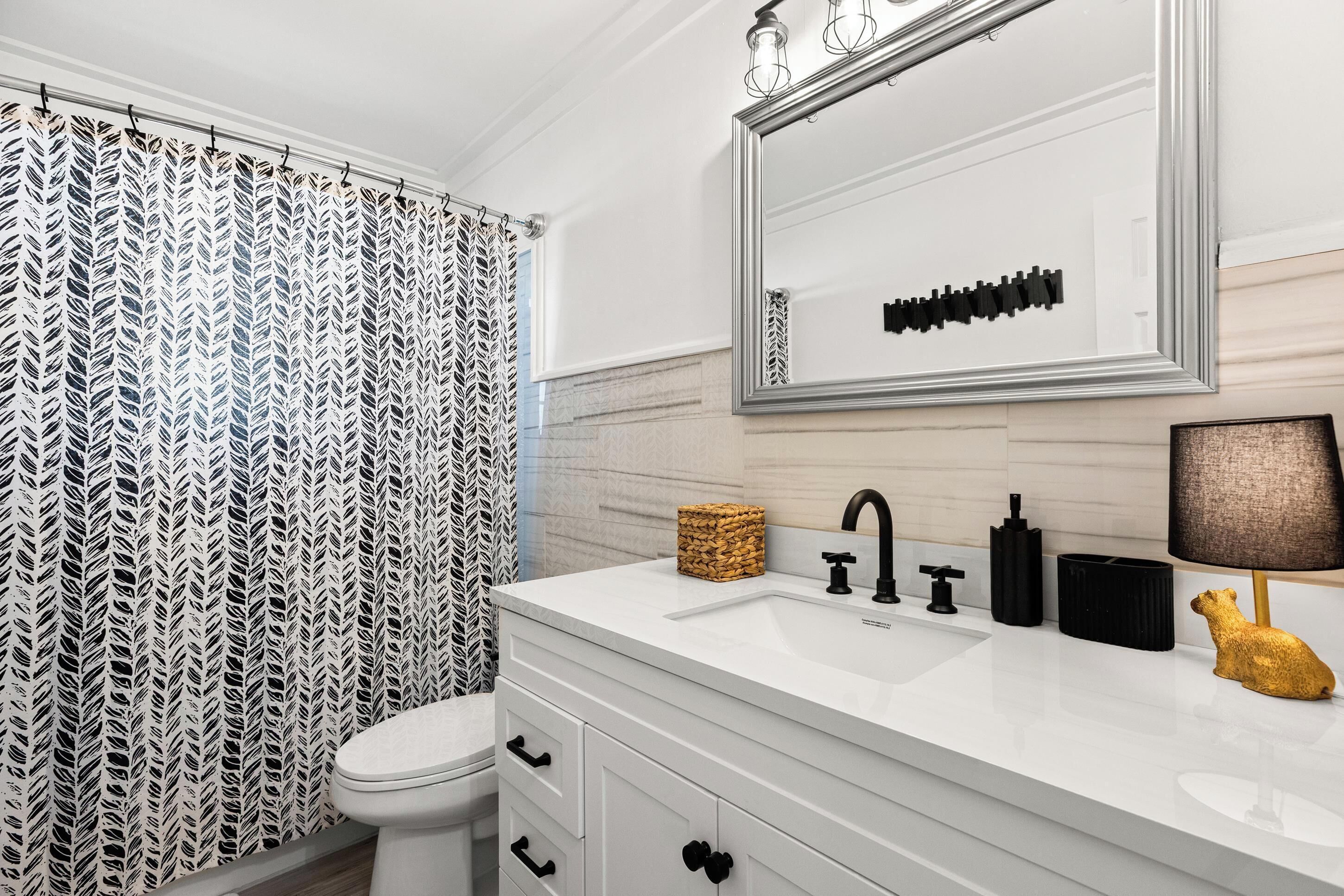 A bathroom with a white vanity, a mirror, a toilet, and a shower curtain.