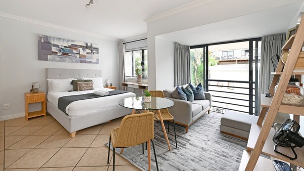 Ein modernes Hotelzimmer mit Bett, einer Couch, einem Esstisch und einem großen Fenster.