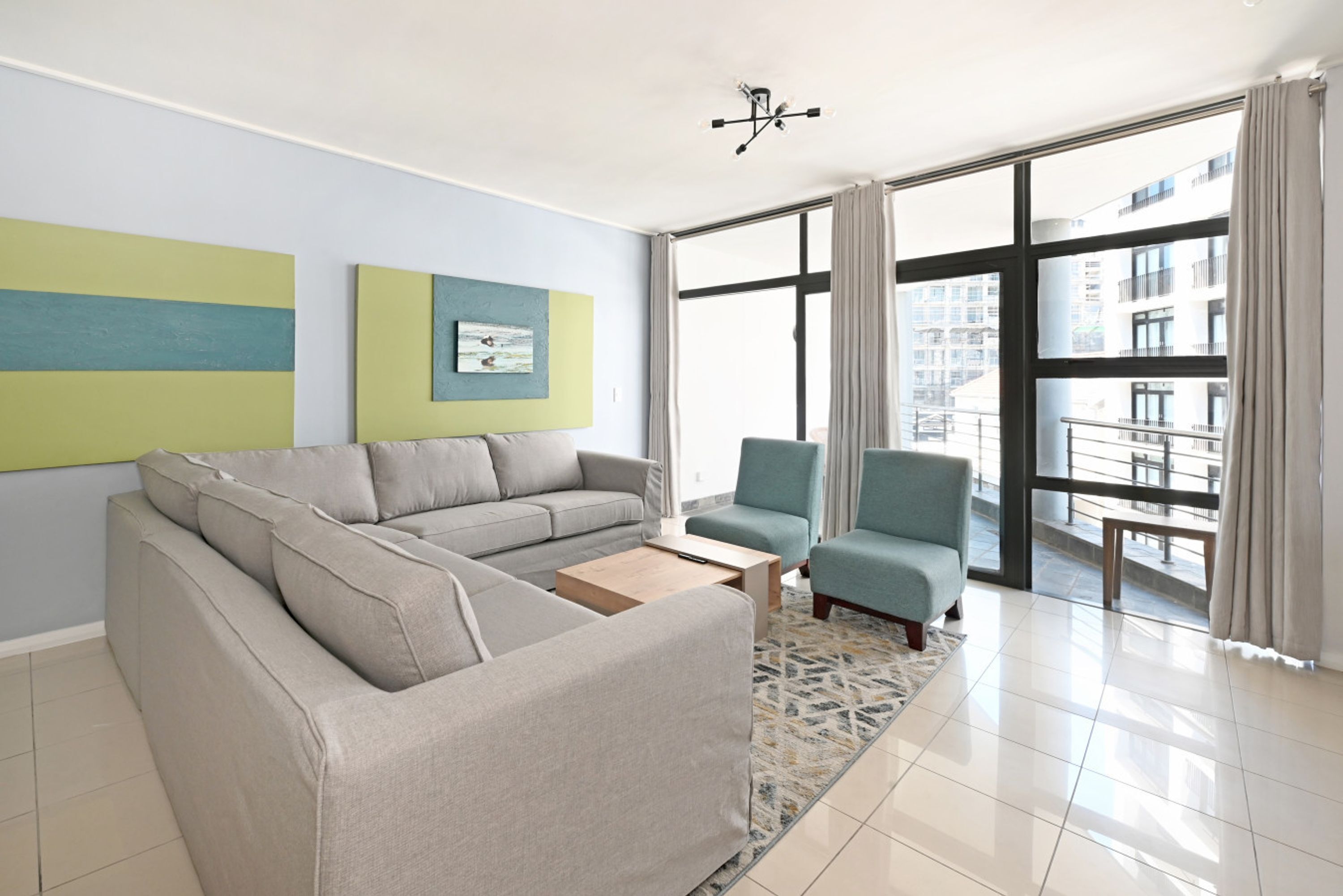 Una sala de estar moderna con un sofá modular, dos sillones, una mesa de centro y un ventanal con vistas a edificios.