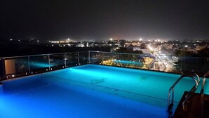 A rooftop pool with a glass railing and a city view at night. - HOTEL AVINASH INTERNATIONAL (Jagdalpur)