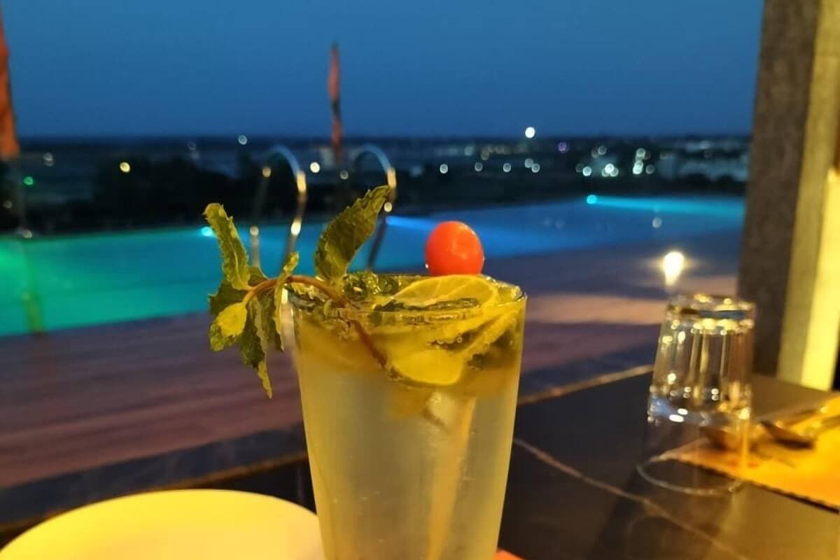 A cocktail with a garnish, a menu, and a view of the sea at dusk.