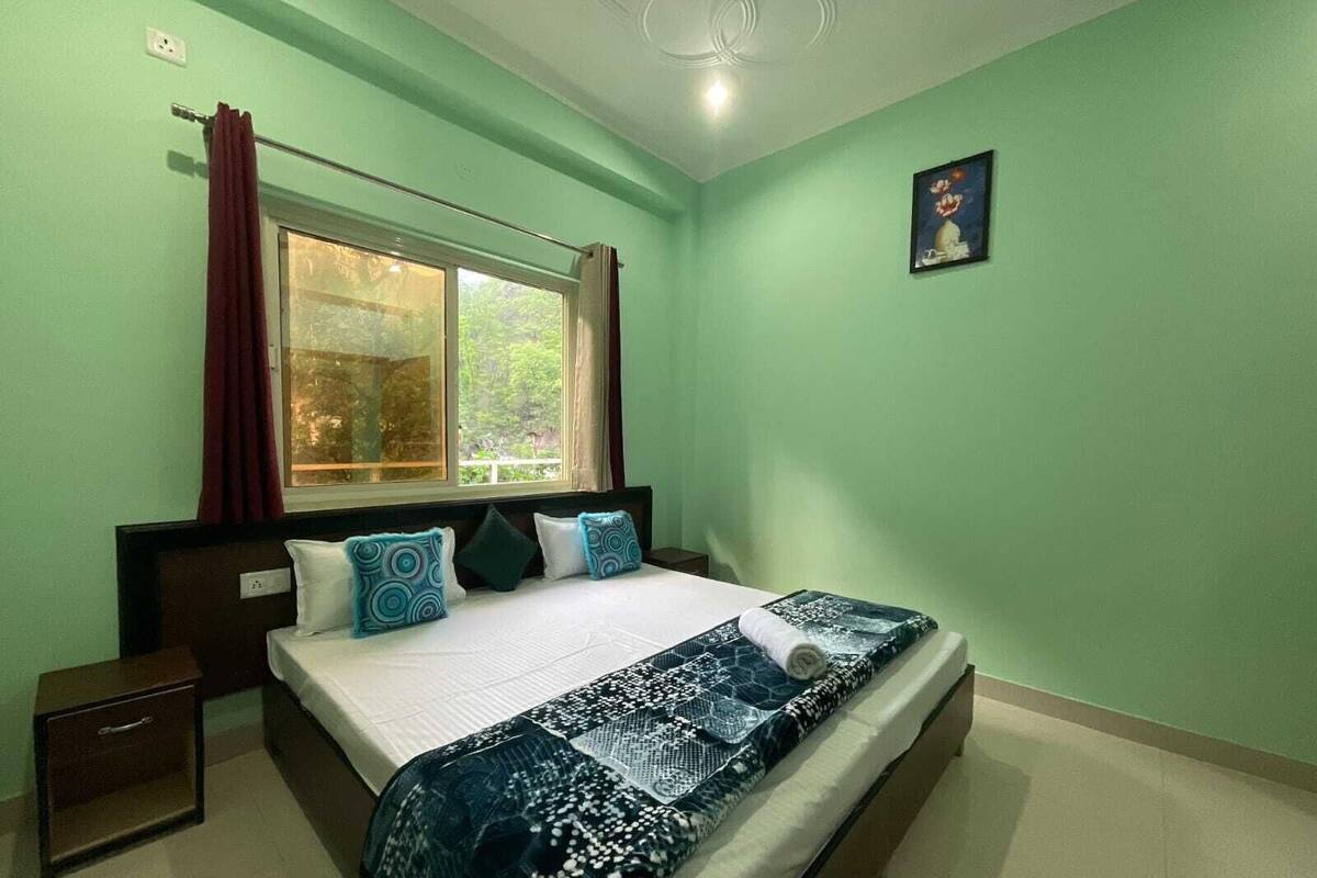 A bedroom with a bed, a nightstand, a window with curtains, and a painting on the wall.