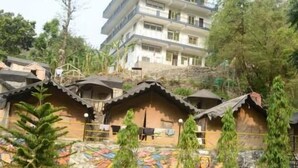 A courtyard with traditional huts, a pool, and a multi-story building in the background. - Hotel The Rudram Aura  (Rishikesh)