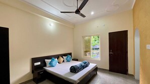 A bedroom with a bed, nightstands, a ceiling fan, a window, and a door. - Hotel The Rudram Aura  (Rishikesh)