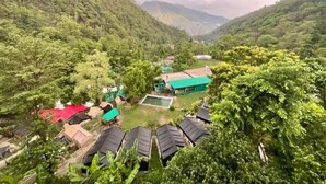 A mountainous area with several buildings, including a green-roofed structure and a red-roofed building. - Hotel The Rudram Aura  (Rishikesh)
