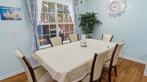 A dining room with a table set for six, a chandelier, a clock, and a window with curtains. - 3br Savannah Home Sleeps 5 Near Historic District 3 Bedroom Home (Savannah)