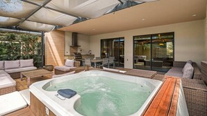 A covered outdoor area with a hot tub, wicker furniture, and a dining table. - Magic Village Resort - Hot Tub & BBQ (Kissimmee)