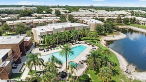 En resort med swimmingpool omgivet af palmer og liggestole, ved siden af et vandareal.