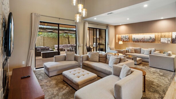 A spacious living room with multiple seating areas, a flat-screen TV, and a large window overlooking a garden. - Magic Village Resort - Hot Tub & BBQ (Kissimmee)