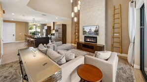 A modern living room with a sofa, a TV, a fireplace, and a dining area. - Magic Village Resort - Hot Tub & BBQ (Kissimmee)