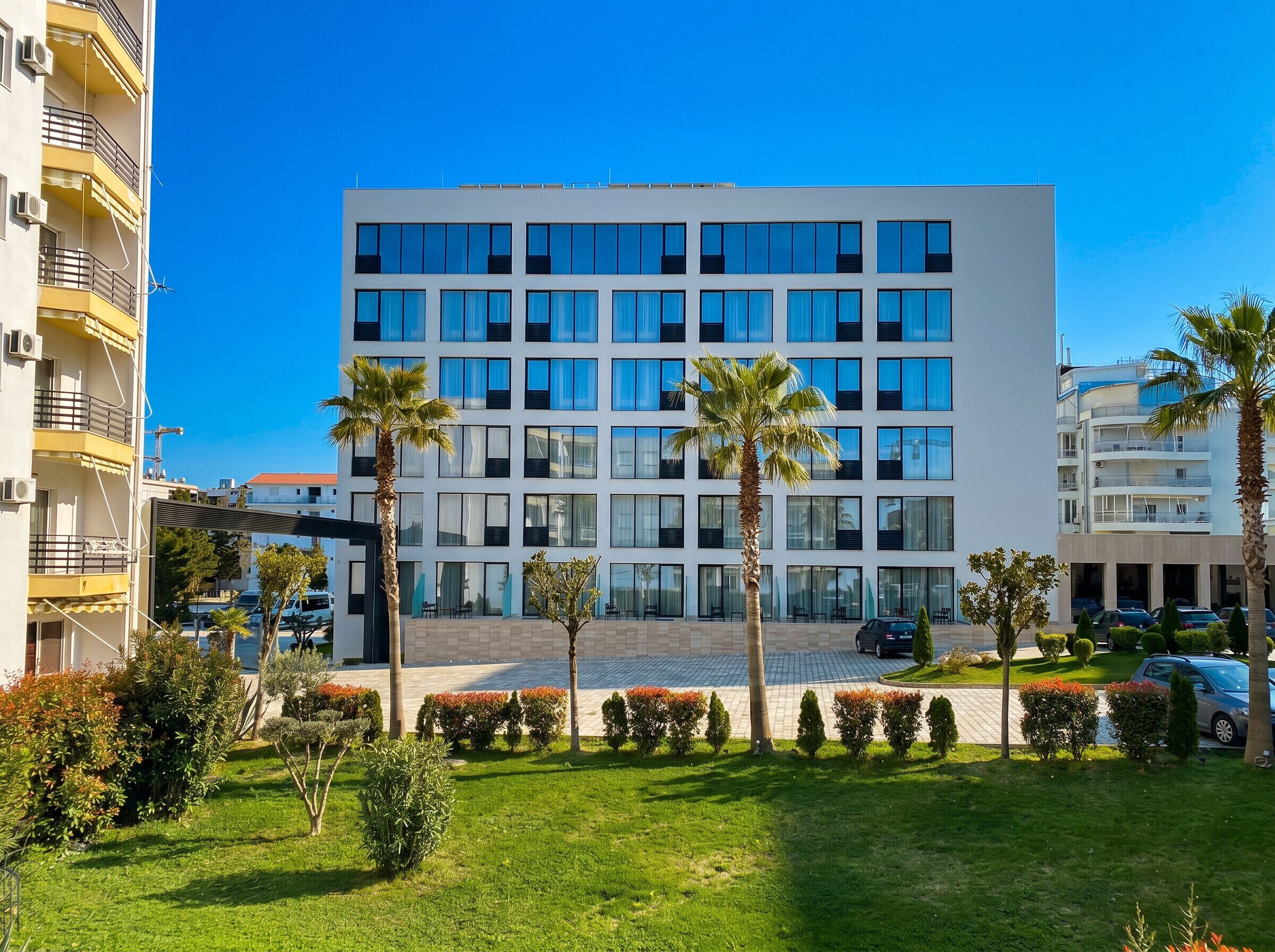 Un hôtel moderne à plusieurs étages, doté d’une cour intérieure, de palmiers et d’un espace de stationnement.