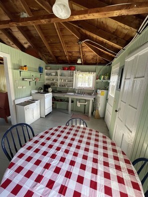 A rustic kitchen with wooden beams, a checkered table, and basic amenities. - Trainor Camp Limit 4 2 Bedroom Cabin (Sebago)