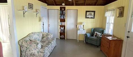 Una habitación con techo de madera, un sofá floral, un sillón rojo, un sillón azul, un aparador de madera y una estantería.
