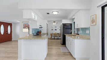 Uma cozinha moderna com armários brancos, uma ilha central e um espaço de jantar com mesa e cadeiras.