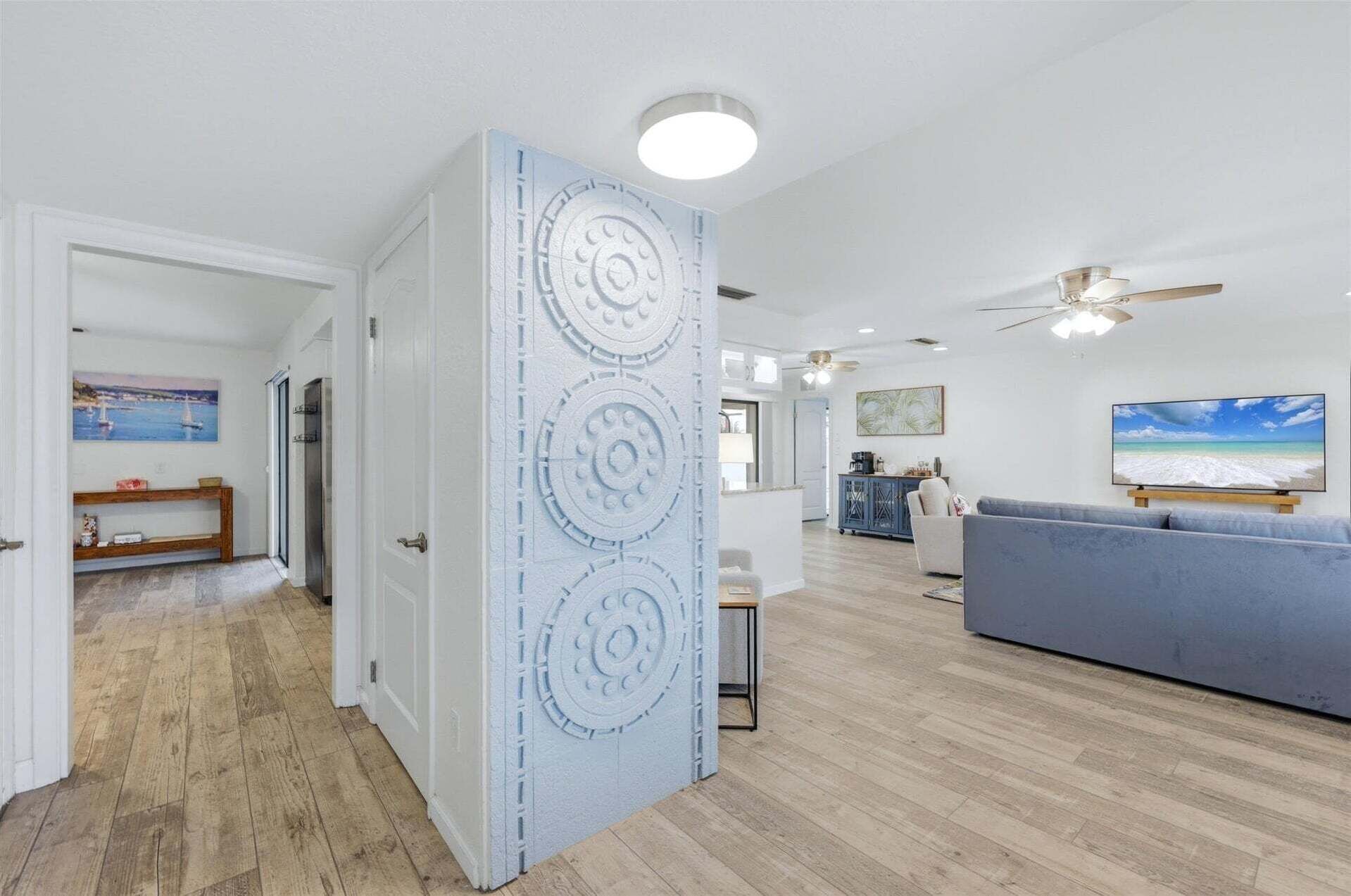 Un vaste espace de vie comprenant un grand canapé, un ventilateur de plafond et un téléviseur diffusant une scène de plage.