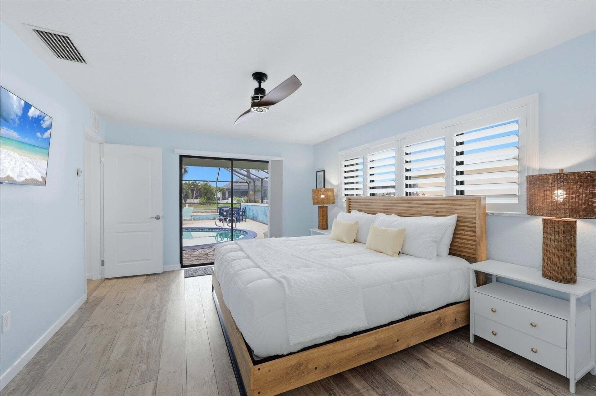 Quarto com cama, mesa de cabeceira, luminária, ventilador de teto e vista para uma piscina.