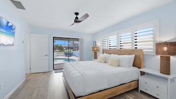 Quarto com cama, mesa de cabeceira, luminária, ventilador de teto e vista para uma piscina.