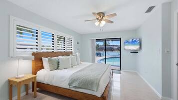 Quarto com cama, ventilador de teto, televisão e vista para uma piscina.