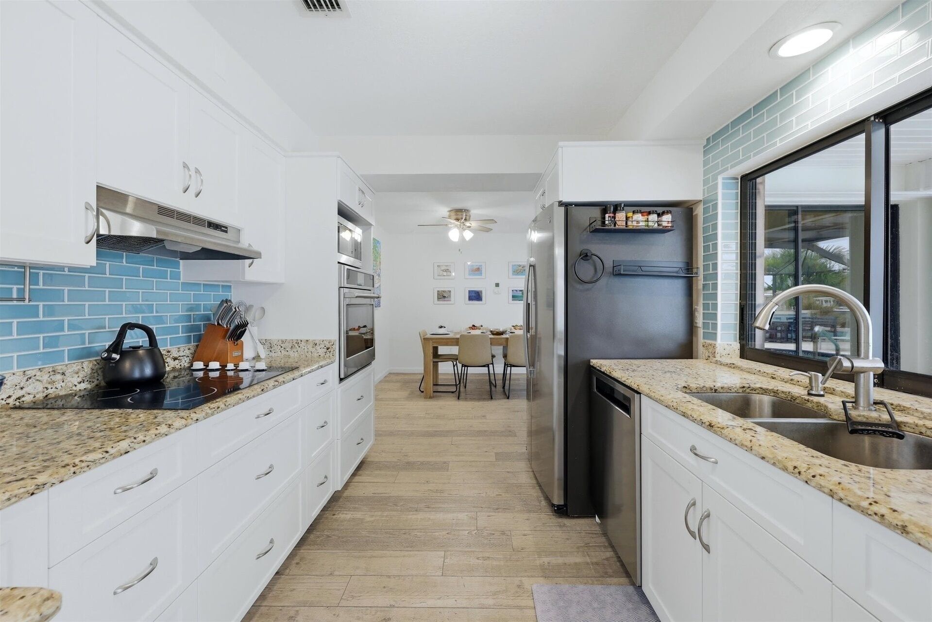 A modern kitchen with white cabinetry, a granite countertop, a stainless steel refrigerator, and a dining area with a table and chairs.