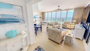 A spacious living area with a large window offering a view of the sea, a dining area with a table and chairs, and a seating area with sofas and a lamp. - Silver Beach 0704e 3 Bedroom Condo (Destin)