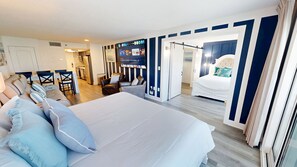 A hotel room with a large bed, a seating area with chairs, a dining table, and a kitchen in the background. - Islander Beach Resort 407 1 Bedroom Condo (Fort Walton Beach)