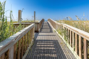 A wooden boardwalk leading to a beach, surrounded by tall grass and clear blue sky. - Islander Beach Resort 407 1 Bedroom Condo (Fort Walton Beach)