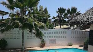 A swimming pool with a sign, palm trees, and a stone patio. - Punda Milia Paradise Hotel Shanzu (Mombasa)