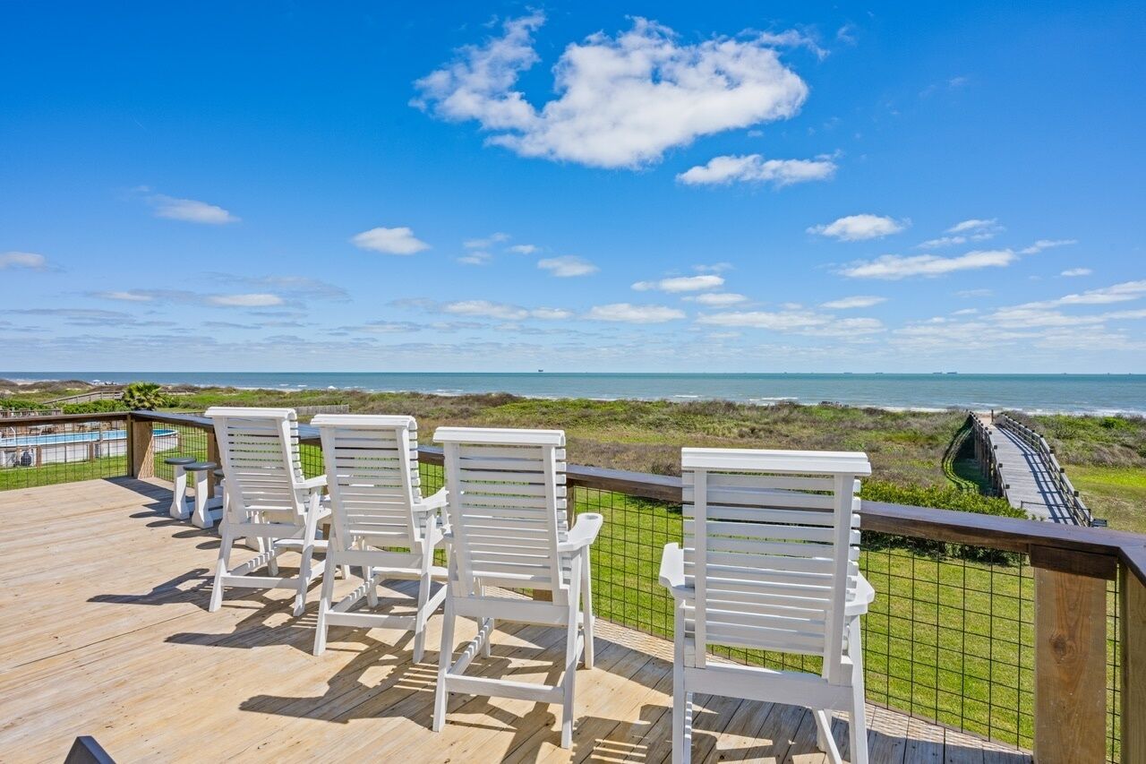Een terras met witte stoelen met uitzicht op een strand en een promenade.