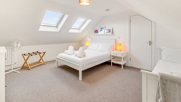 A bedroom with a bed, bedside tables, a fan, a drying rack, and skylights. - Helens Place - North East Escapes (Whitley Bay)