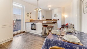 A modern kitchen with a dining area, wooden flooring, and a table set for four. - Helens Place - North East Escapes (Whitley Bay)