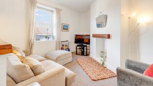 A living room with a sofa, ottoman, TV, and a rug. - Helens Place - North East Escapes (Whitley Bay)