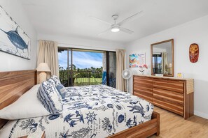 A bedroom with a bed, a wooden dresser, a ceiling fan, a large window, and a view of the outdoors. - Keauhou Punahele B-207 Ocean Views, Spacious Lanai, Personal BBQ, No Stairs (Kailua Kona)