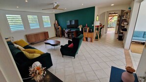 A living room with a sofa, armchair, coffee table, and a TV. There are bookshelves and a dining area visible in the background. - Villa Ti Kaz a Mymy - Pool villa St-François (Saint-François)