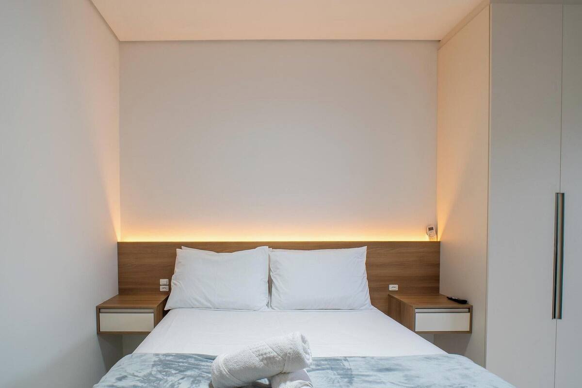 A minimalist hotel room with a bed, two bedside tables, and a nightstand with a lamp.
