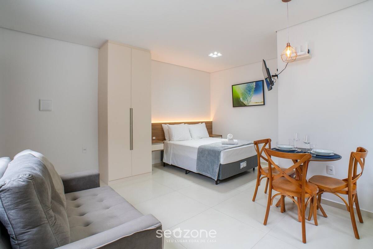 A modern bedroom with a bed, bedside table, and a dining area with chairs and a table.