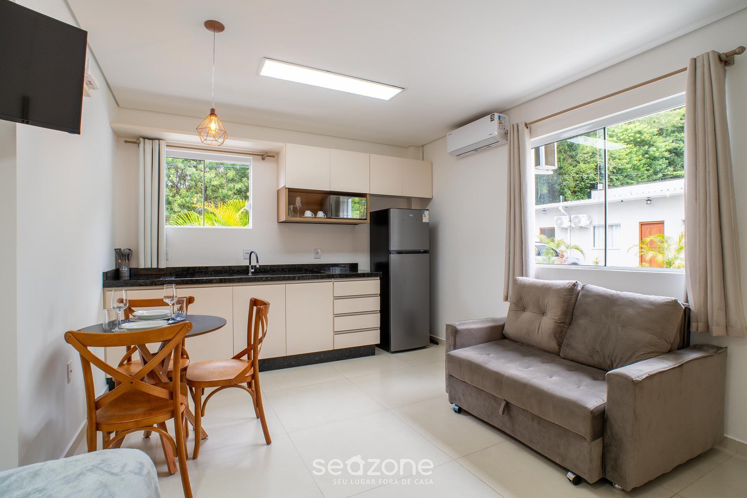 Un espacio habitable compacto con kitchenette, comedor, sofá y ventanas grandes.