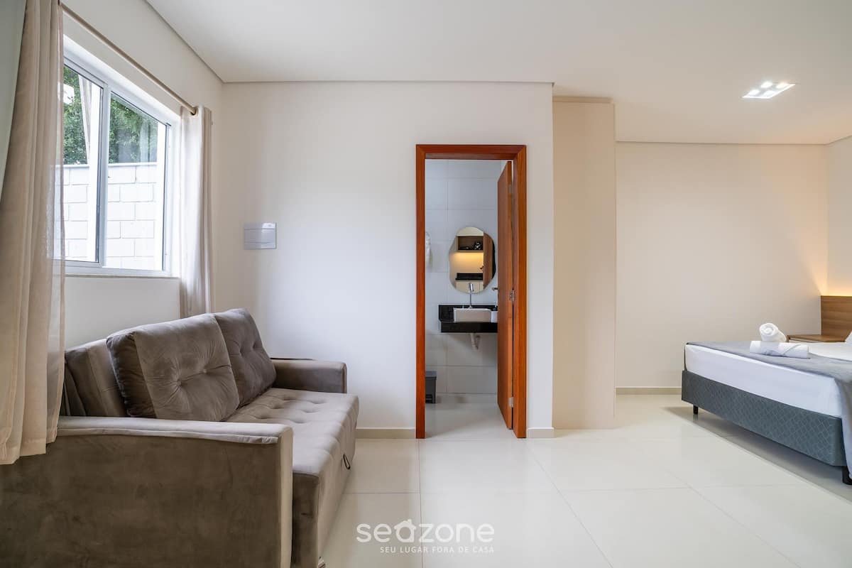 A hotel room with a sofa, a bed, a bathroom with a mirror, and a view through an open door.