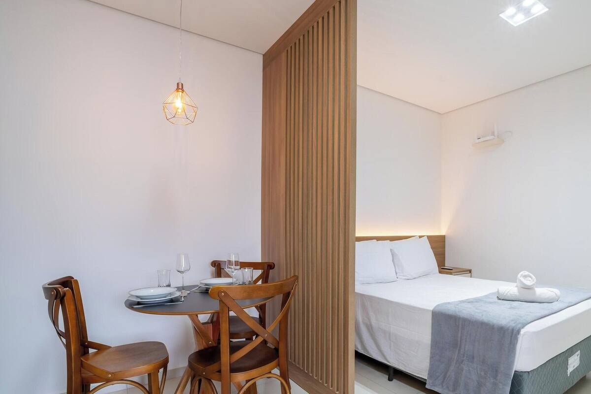 A hotel room with a bed, bedside table, and a dining area with chairs and a table.