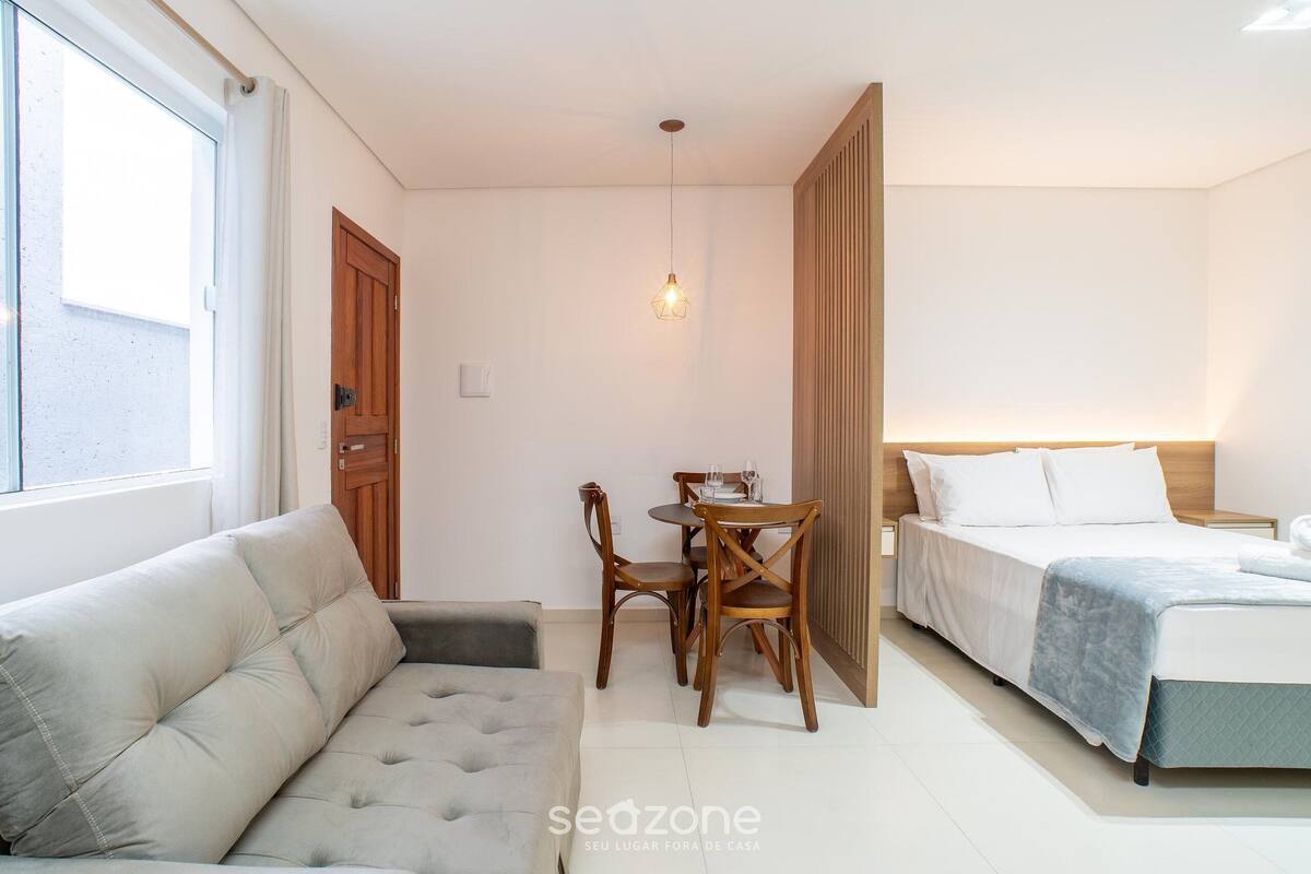 A bedroom with a bed, a sofa, a dining table with chairs, and a hanging light fixture.
