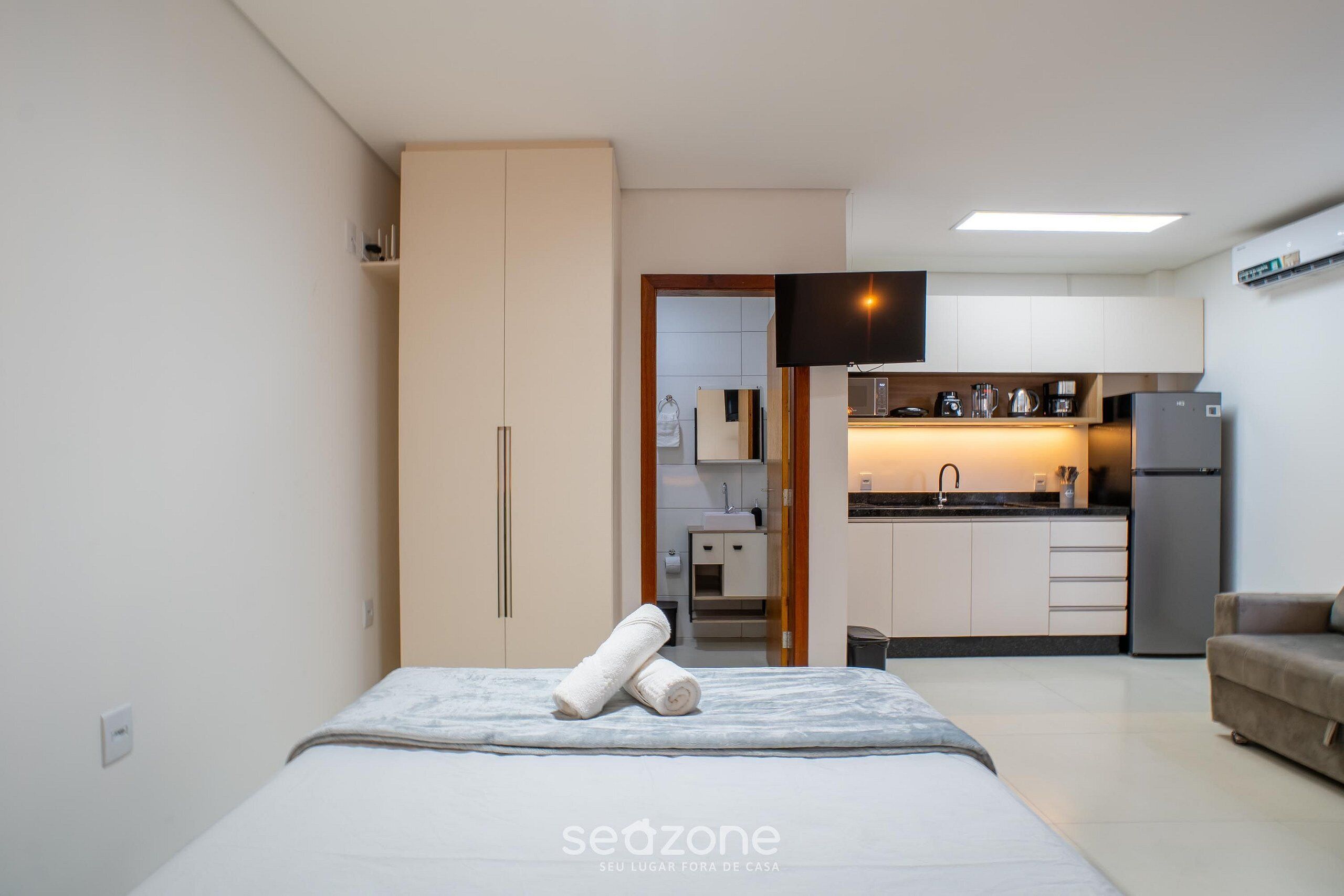 Quarto moderno com cama, sofá, cozinha e TV.