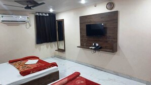 Habitación de hotel con cama, televisor montado en un panel de madera, equipo de aire acondicionado y ventilador de techo.