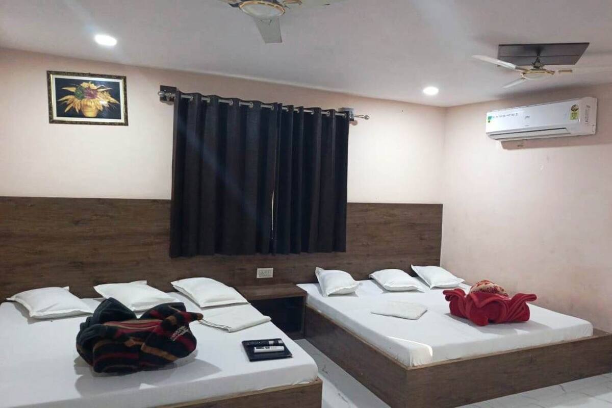 A hotel room with two single beds, a ceiling fan, an air conditioning unit, and a framed picture on the wall.