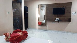 Habitación de hotel con cama, televisor montado en un panel de madera, espejo y una toalla roja en el suelo.
