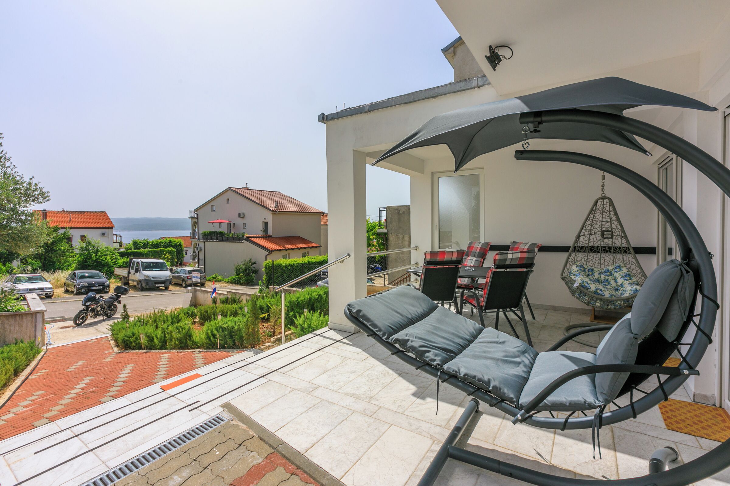 En balkon med en hængestol, et bord med stole og havudsigt.