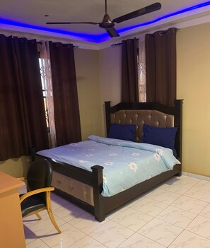 A bedroom with a bed, a chair, a ceiling fan, and curtains.